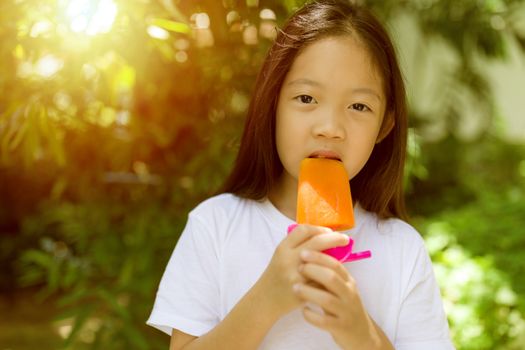 Happy Asian child eating popsicle ice cream during hot summer day.