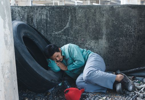 An Asian homeless man is sitting by the wall. His face is full of suffering, depression and despair. People are unemployed due to the effects of the corona virus outbreak.