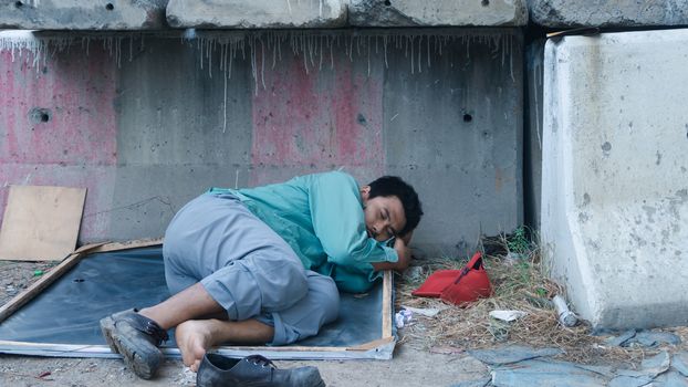 Asian homeless man lying beside the wall His face is full of suffering, depression, and despair. People are unemployed due to the effects of the corona virus outbreak.