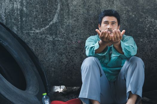 An Asian homeless man is sitting by the wall. His face is full of suffering, depression and despair. People are unemployed due to the effects of the corona virus outbreak.