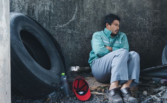 An Asian homeless man is sitting by the wall. His face is full of suffering, depression and despair. People are unemployed due to the effects of the corona virus outbreak.