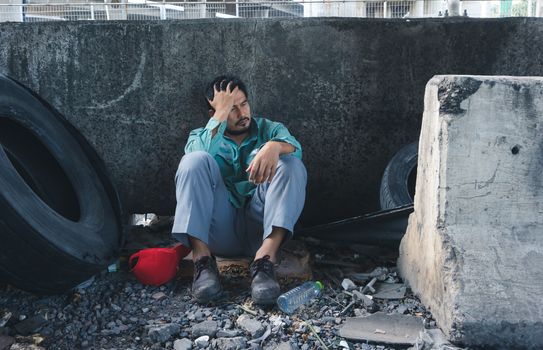 An Asian homeless man is sitting by the wall. His face is full of suffering, depression and despair. People are unemployed due to the effects of the corona virus outbreak.