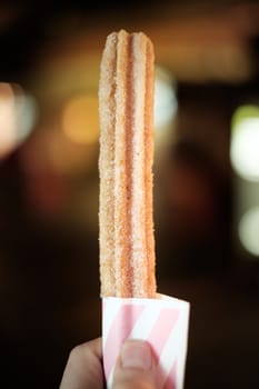 Churro dessert held by hand with bokeh background.