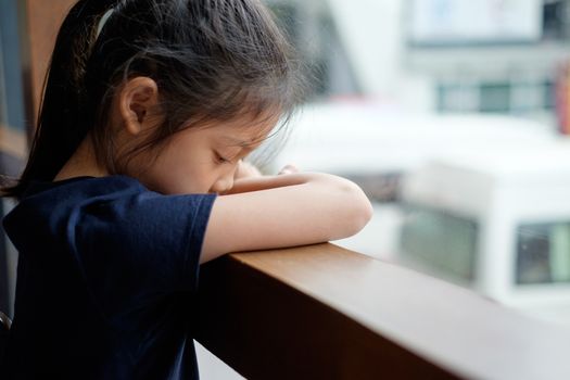 Sad and lonely Asian child sits next to window.