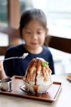 Happy Asian child enjoys eating Korean Patbingsu or Bingsu, shave ice frozen dessert.