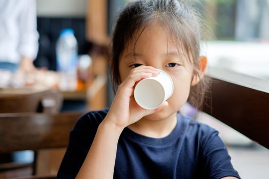 Asian child drinks water from white paper cup.