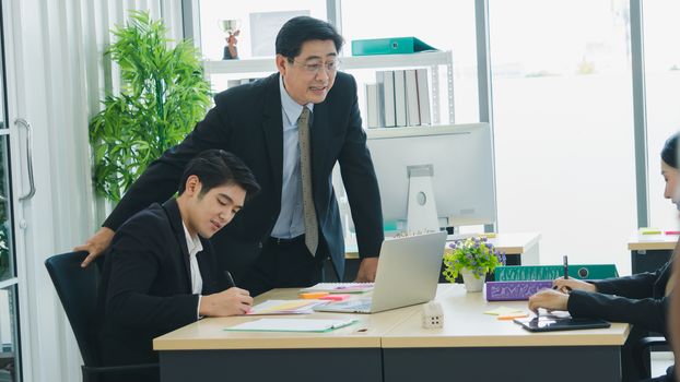 The Asian business team is working together happily at the office. Senior male business men are teaching a new generation of business people