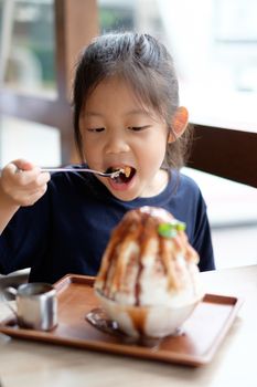 Happy Asian kid enjoys eating shave ice frozen dessert.
