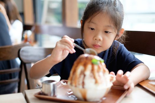 Happy Asian child enjoys eating Korean Patbingsu or Bingsu, shave ice frozen dessert.