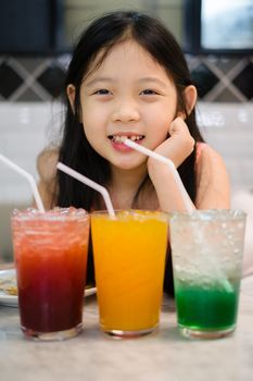 Little Asian child drinking fruit juice beverage from glass.