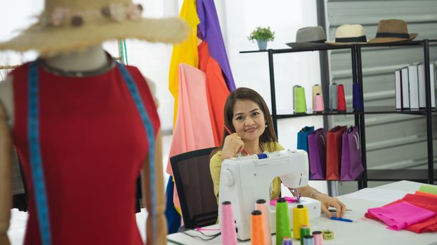 An Asian female fashion designer is working and smiling happily. Small businesses work from home.