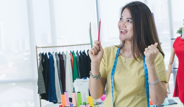 An Asian female fashion designer is working and smiling happily. Small businesses work from home.