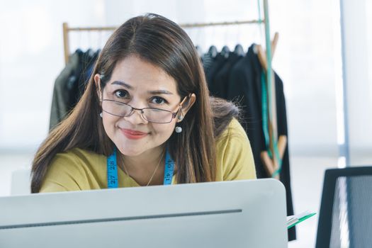 An Asian female fashion designer is working and smiling happily. Small businesses work from home.