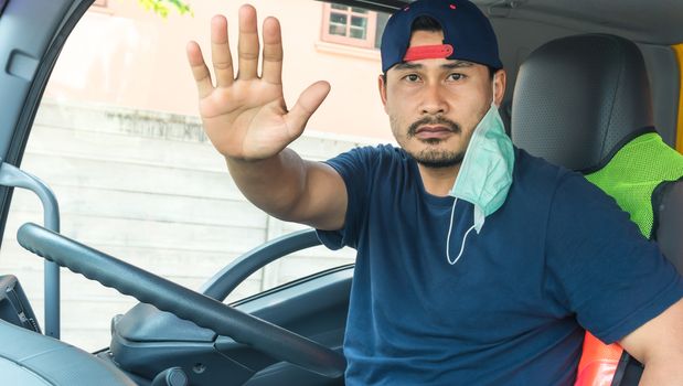 An Asian male truck driver with a dust and virus mask was sitting, raising his hands to stop in the front of the car to prevent the spread of the corona virus, Covid-19.