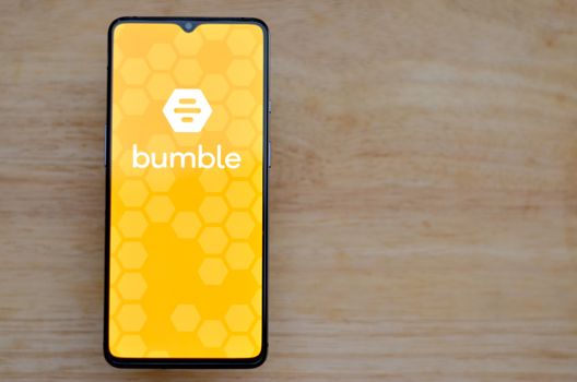 London, England, United Kingdom, 2020. Flat lay with wooden background and Bumble app logo on display on a smartphone screen. Bumble is an online social search and dating mobile app