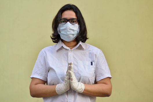 Portrait of young medical healthcare female worker wearing surgical face mask to protect herself from Corona Virus (COVID-19) pandemic against yellow background. Concept : Getting ready to fight