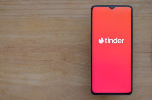 London, England, United Kingdom, 2020. Flat lay with wooden background and Tinder app logo on display on a smartphone screen. Tinder is an online social search and dating mobile app