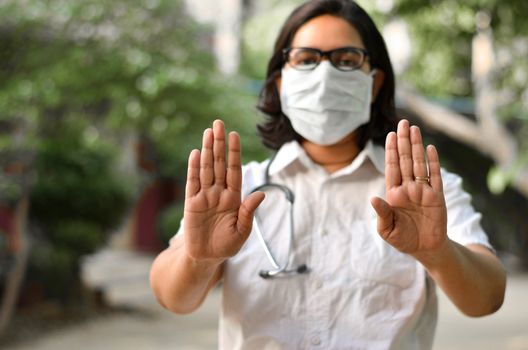 Portrait of young medical healthcare female worker showing her hands out & wearing surgical face mask to protect from Corona Virus (COVID-19) pandemic against blur background.Concept Ready to fight