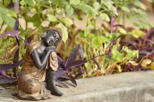 Close up of discarded miniature statue of Buddha kept in a backyard / garden made of black clay / stone