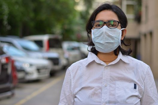 Portrait of a young medical healthcare female worker wearing surgical mask on her face to protect herself from Corona Virus (COVID-19) pandemic against blur background. Concept Ready to fight Covid-19