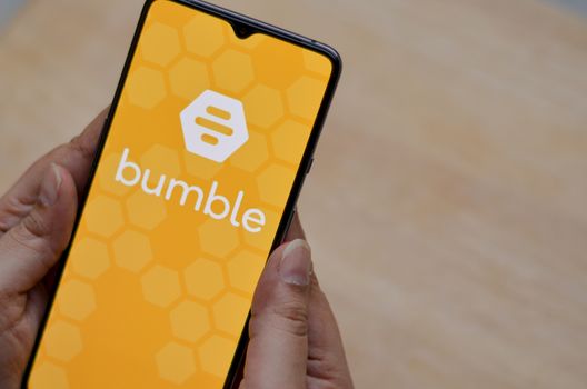 London, England, United Kingdom, 2020. Flat lay with wooden background and Bumble app logo on display on a smartphone screen in female hands. Bumble is an online social search and dating mobile app