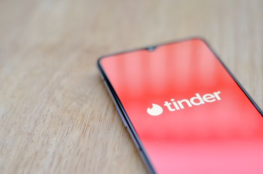 New York, USA, 2020. Flat lay with wooden background and Tinder app logo on display on a smartphone screen. Tinder is an online social search and dating mobile phone app