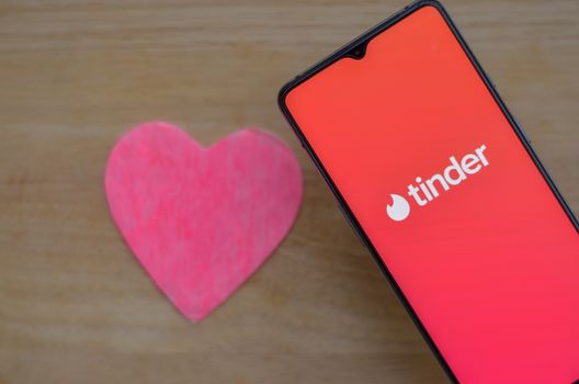 New York, USA, 2020. Flat lay with Tinder app logo on a smartphone screen with a pink heart on a wooden background on display. Tinder is an online social search and dating mobile phone app