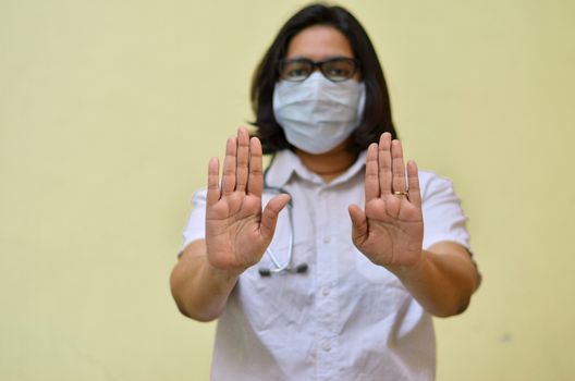 Portrait of young medical healthcare female worker showing her hands out & wearing surgical face mask to protect from Corona Virus (COVID-19) pandemic against yellow background.Concept Ready to fight