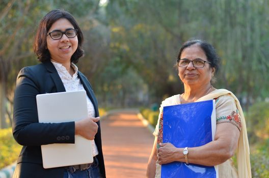 Young Indian entrepreneur woman and her old retired mother standing with a laptop and file in their hand's in a park in Delhi. Concept - Women entrepreneurs from India , Education, Digital Literacy