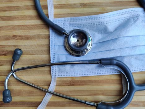 White breathable surgical face mask and stethoscope on a white background denoting doctor's Corona virus (Covid-19) safety kit to reduce the rate of spread of infections against a wooden background