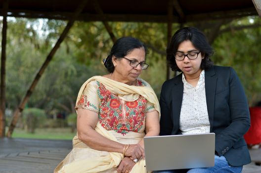 Young Indian woman helping her old retired mother on a laptop sitting in a park in New Delhi, India. Concept - Digital literacy / Education, Mother's Day