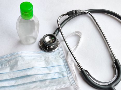 White breathable surgical face mask, sanitizer and stethoscope on a white background denoting doctor's Corona virus (Covid-19) safety kit to reduce the rate of spread of infections