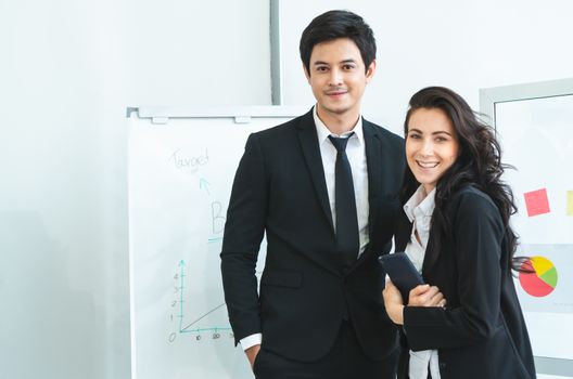 A photograph of a young Asian businessman and a Caucasian businesswoman wearing a black suit working together in an office.