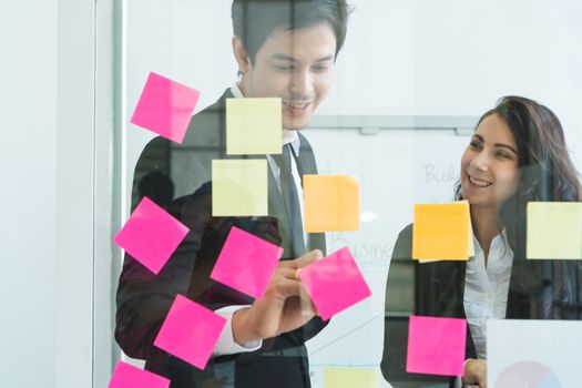 A photograph of a young Asian businessman and a Caucasian businesswoman wearing a black suit working together in an office.