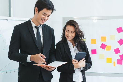 A photograph of a young Asian businessman and a Caucasian businesswoman wearing a black suit working together in an office.