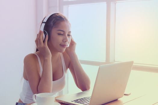 Picture of a beautiful girl in a white dress, sitting by the coffee and listening to music happily by the window.