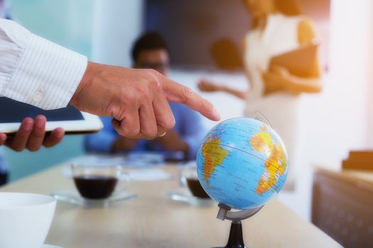 Portrait of businessman pointing his finger at the globe to determine a business investment point with a backdoor is a meeting.