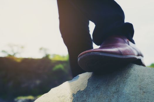 Photo of hipster men's fashion shoes in brown suede shoes walking on rocks in bright weather.