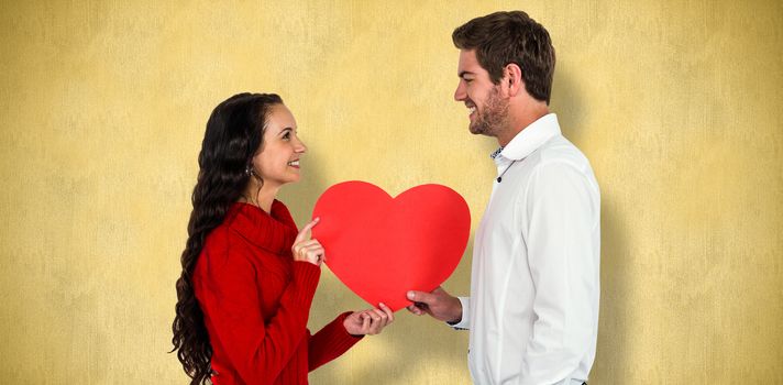 Smiling couple holding paper heart against orange background 