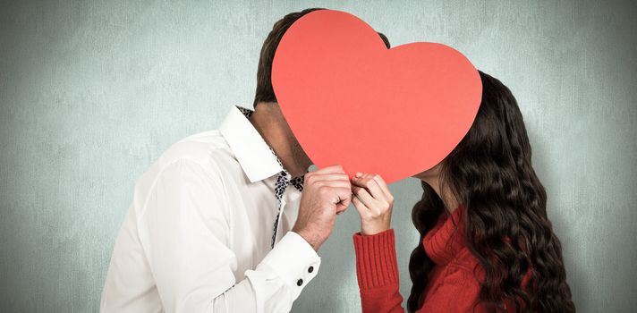 Couple covering faces with paper heart against blue background