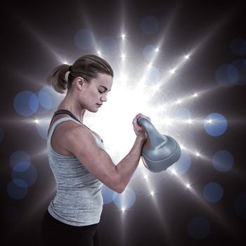 Serious muscular woman lifting kettlebell  against spotlights
