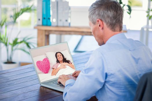 Woman lying in her bed next to a pink heart pillow against businessman working with laptop computer 