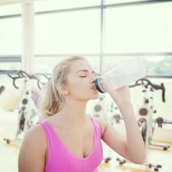 Beautiful healthy woman drinking water against spinning exercise bikes in gym room