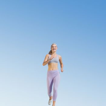 Sporty blonde jogging towards camera against blue sky