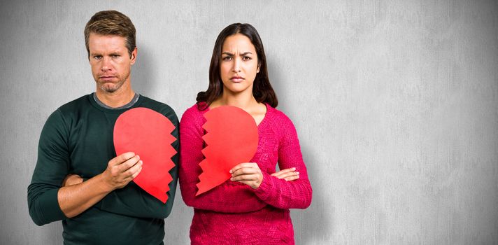 Portrait of serious couple holding cracked heart shape  against white and grey background