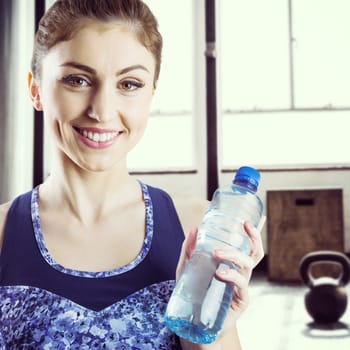 Fit brunette holding water bottle against weights on the studio floor