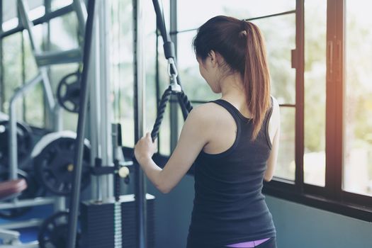 Beautiful girl exercises by pulling the rope to strengthen the muscles in the public gym. Strength training of the arm muscles. Health care concept