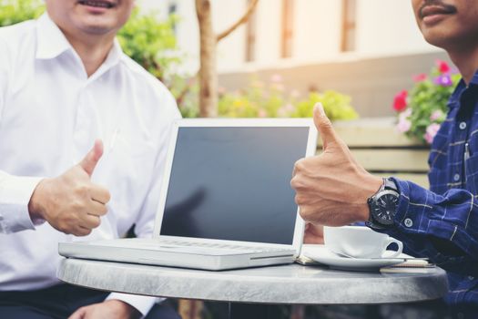 Businessmen are negotiating a casual business in a coffee shop and holding a thumbs up.