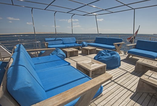 Stern teak sundeck of a large luxury motor yacht with chairs sofa table and tropical sea view background