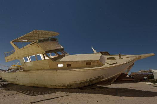 Abandoned derelict wooden boats in the desert under a night sky with abstract lighting effects